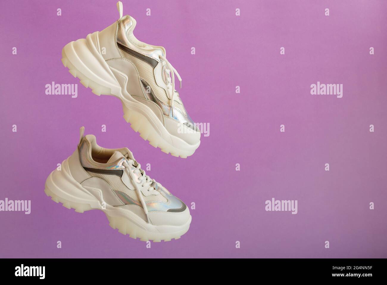 Le sneaker al neon bianco urbano volano su sfondo viola a colori con spazio per la copia. Scarpe da ginnastica bianche levitazione. Paio di sneaker sportive femminili. Foto Stock