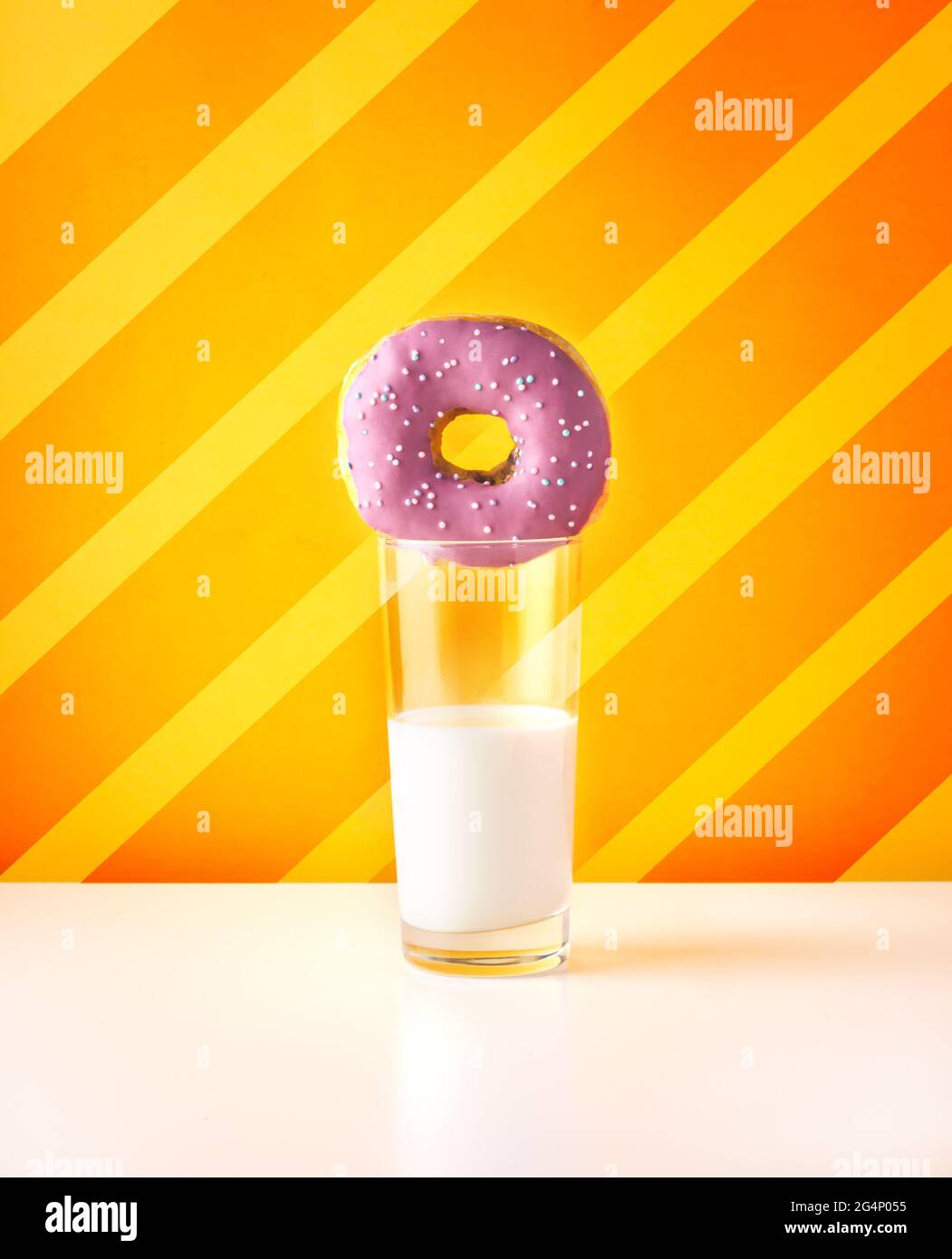 Ciambella viola con un bicchiere di latte vegetale sano su fondo giallo e arancione a strisce. Pubblicità di fast food o copertina di un libro culinario vivace Foto Stock