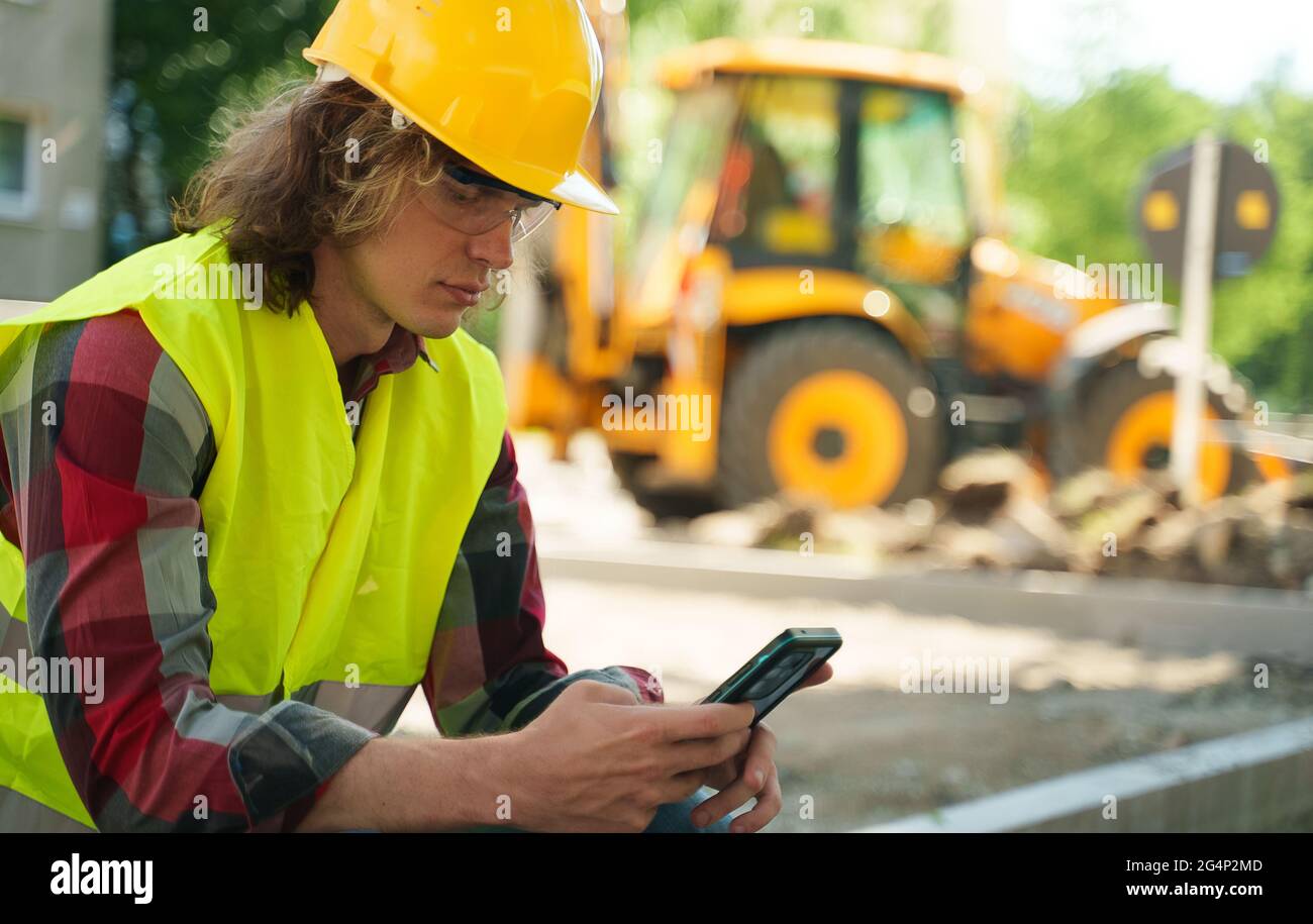 Lavoratore maschile in elmetto e giacca ad alta visibilità con smartphone. Foto Stock