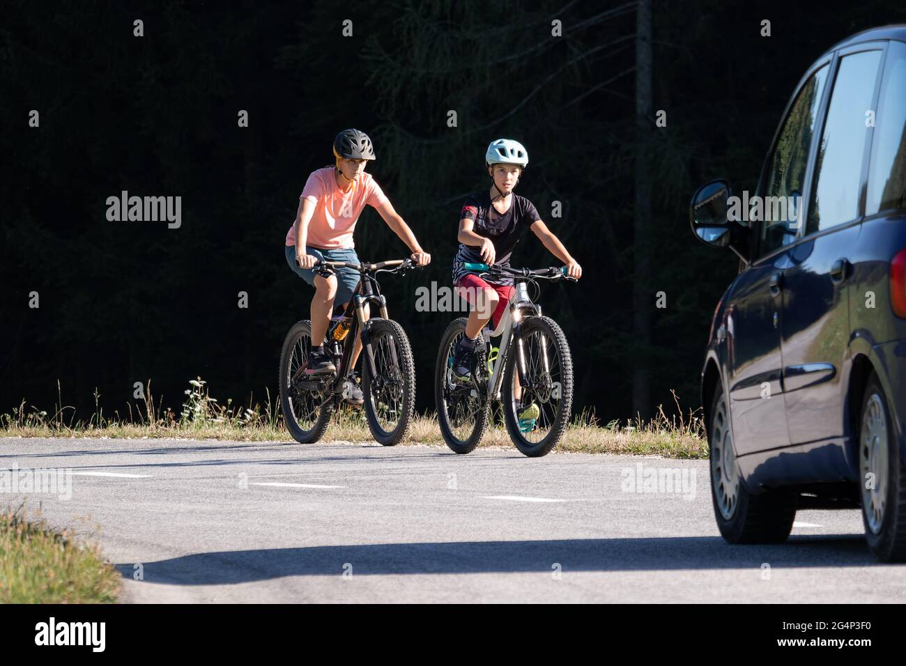 Auto e due ciclisti femminili in pericolo su una strada trafficata con auto che guida verso di loro. Foto Stock
