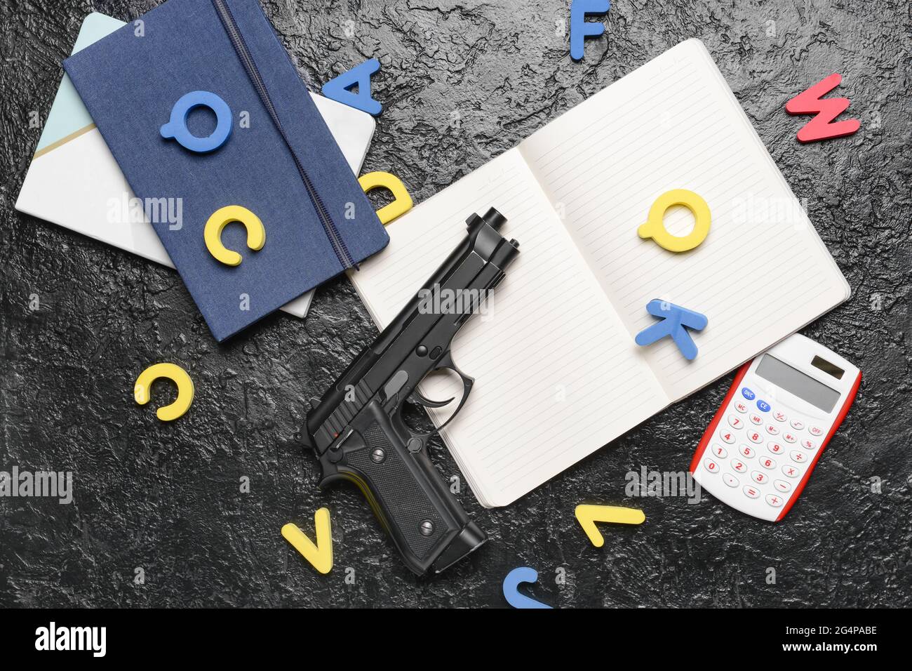 Pistola e cancelleria su sfondo scuro. Concetto di ripresa scolastica Foto Stock