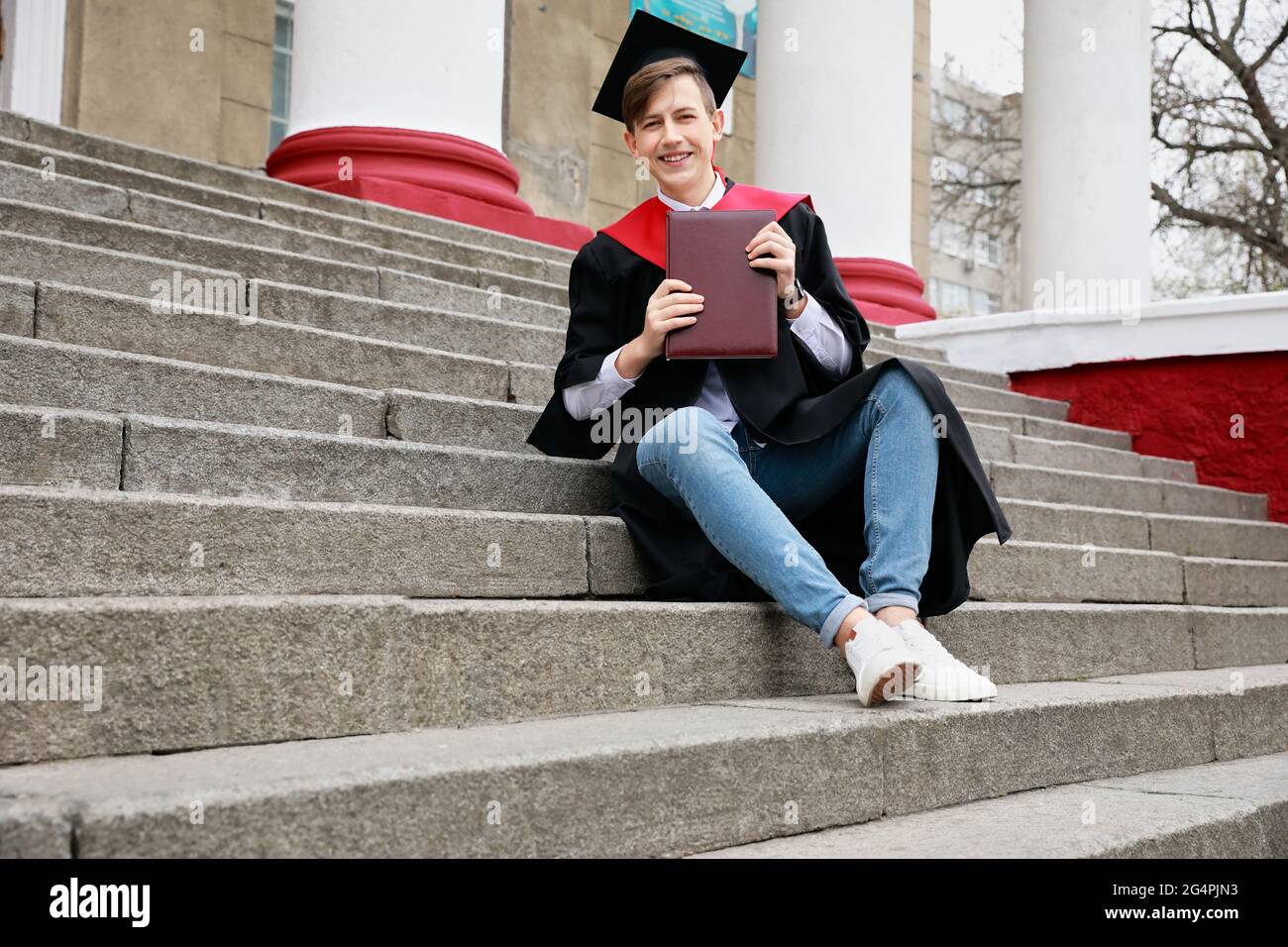 Studente di laurea maschile seduto sulle scale all'aperto Foto Stock