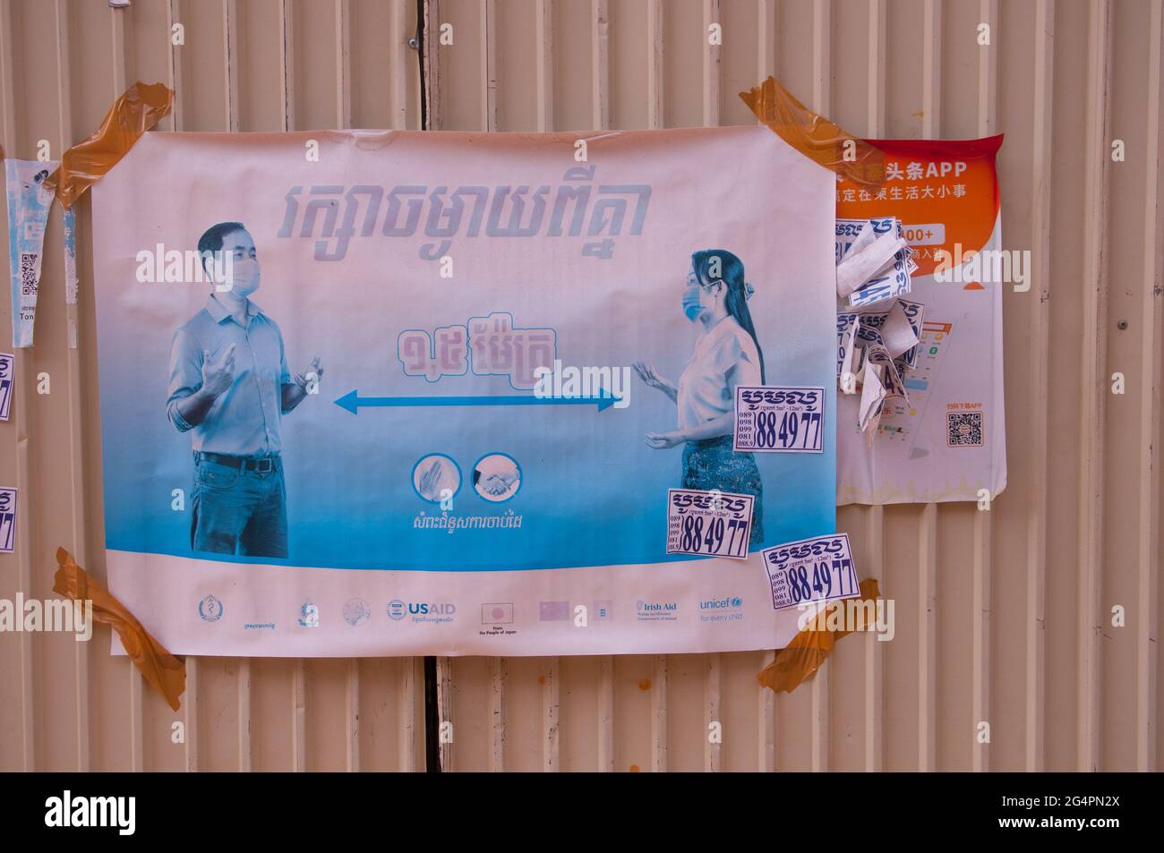 Durante uno scoppio di COVID - 19, USAID mette in su i manifesti in scritto di Khmer, avvertendo i cambogiani circa l'allontanamento sociale & di indossare le maschere della faccia, in una baraccopoli durante la pandemia del coronavirus. Phnom Penh, Cambogia. 15 Marzo 2021. © Kraig Lieb Foto Stock