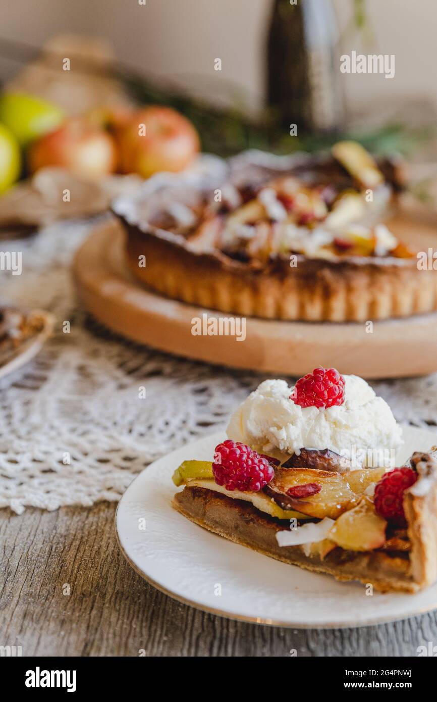 Torta di mele rustica, servita con gelato e frutti di bosco con fiori da tavola. Servito su un piatto di legno pigro Susan. Foto Stock