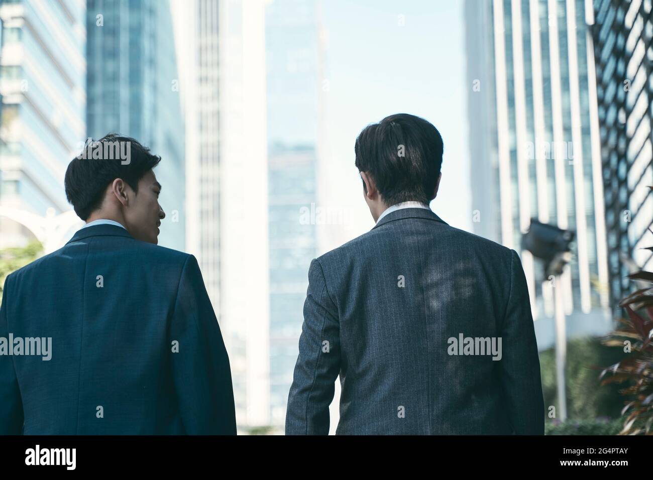 vista posteriore di due uomini d'affari asiatici che camminano parlando nel quartiere centrale degli affari nella città moderna Foto Stock