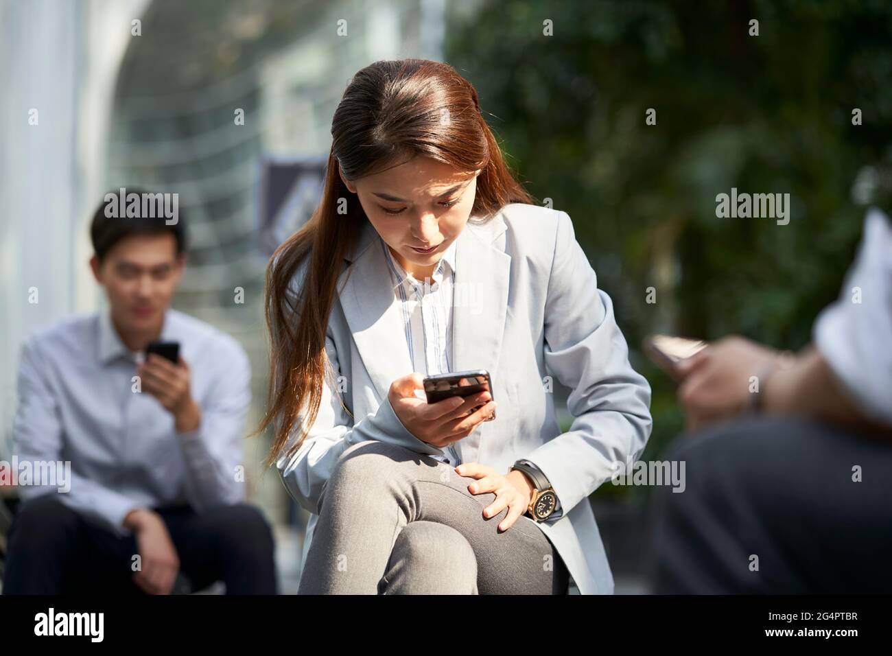 gli uomini d'affari asiatici che usano il concetto esterno del cellulare per la dipendenza dei social media Foto Stock