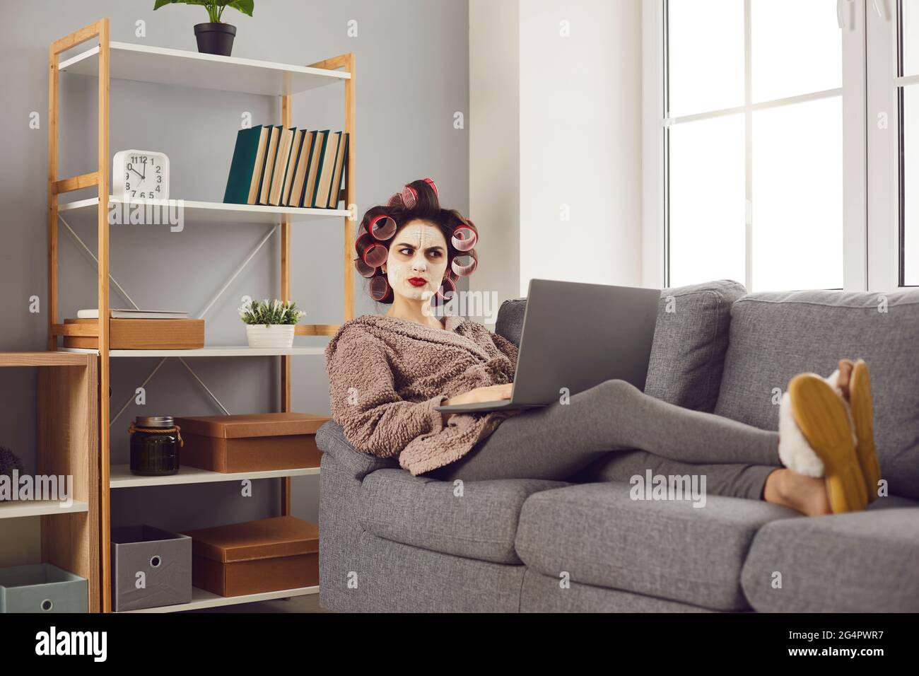 Divertente donna arrabbiata seduta sul divano con il computer portatile e leggere i commenti nasty sui social media Foto Stock