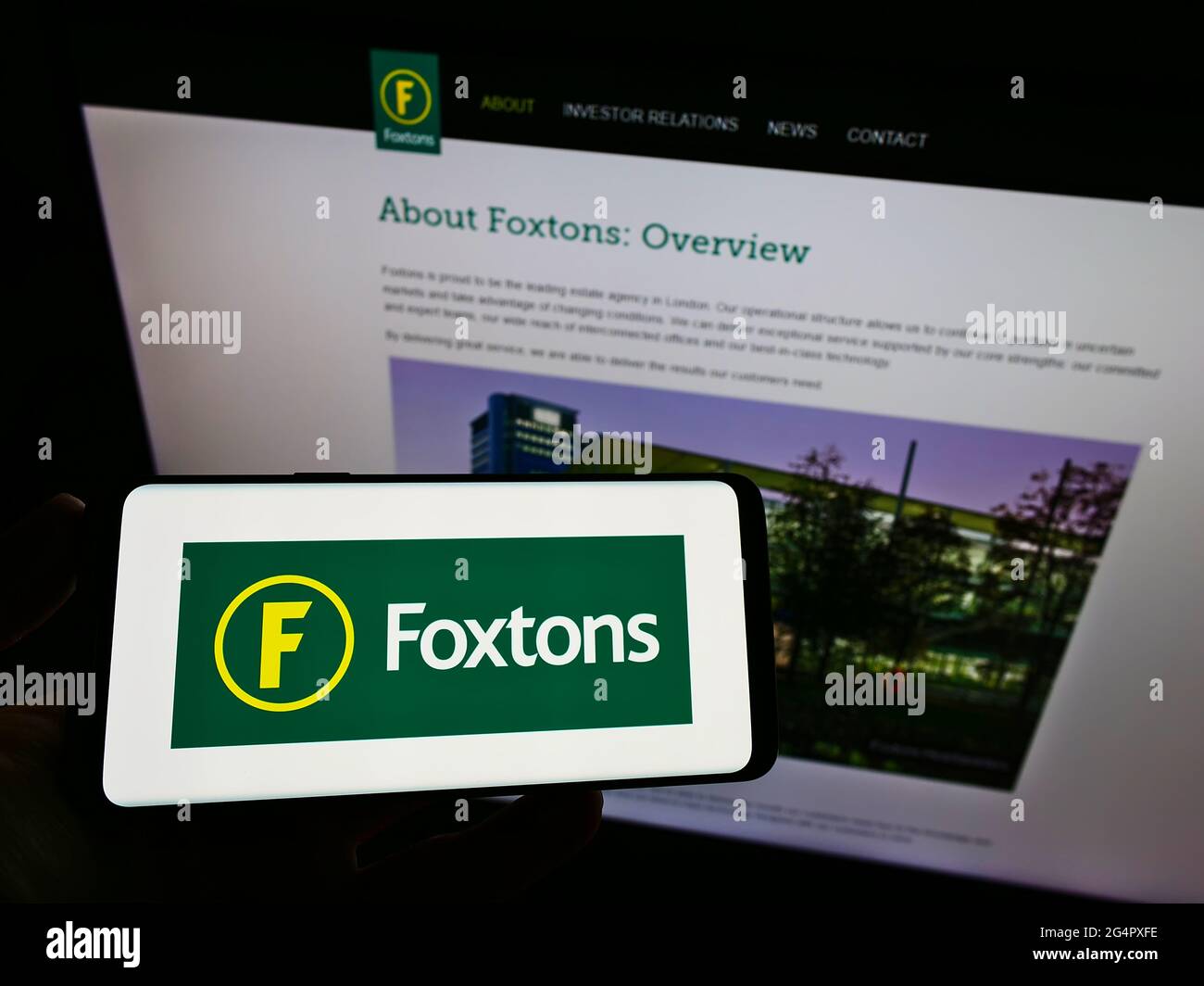 Persona in possesso di smartphone con logo dell'agenzia immobiliare britannica Foxtons Group plc sullo schermo di fronte al sito web. Mettere a fuoco il display del telefono. Foto Stock