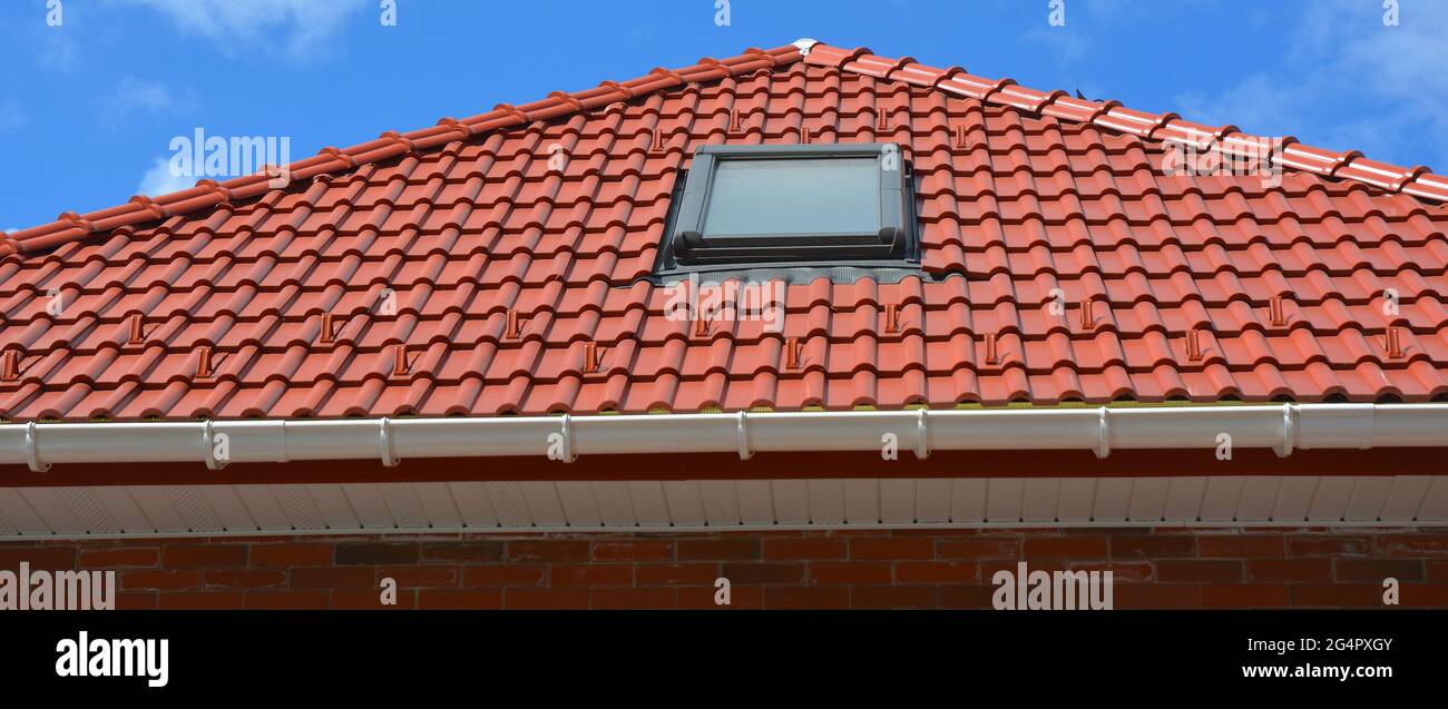 Costruzione di tetti. Tetto in tegole rosse con lucernario installato, gocciolatoio in plastica, plancia e soffito. Foto Stock