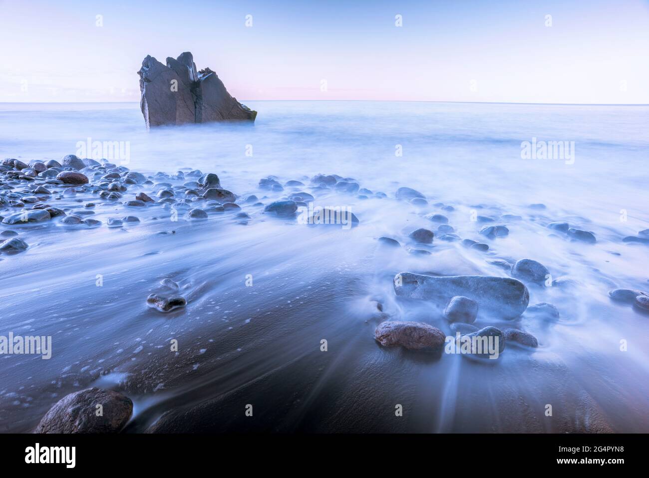 spiaggia vuota dell'oceano all'alba con formazione rocciosa sullo sfondo Foto Stock