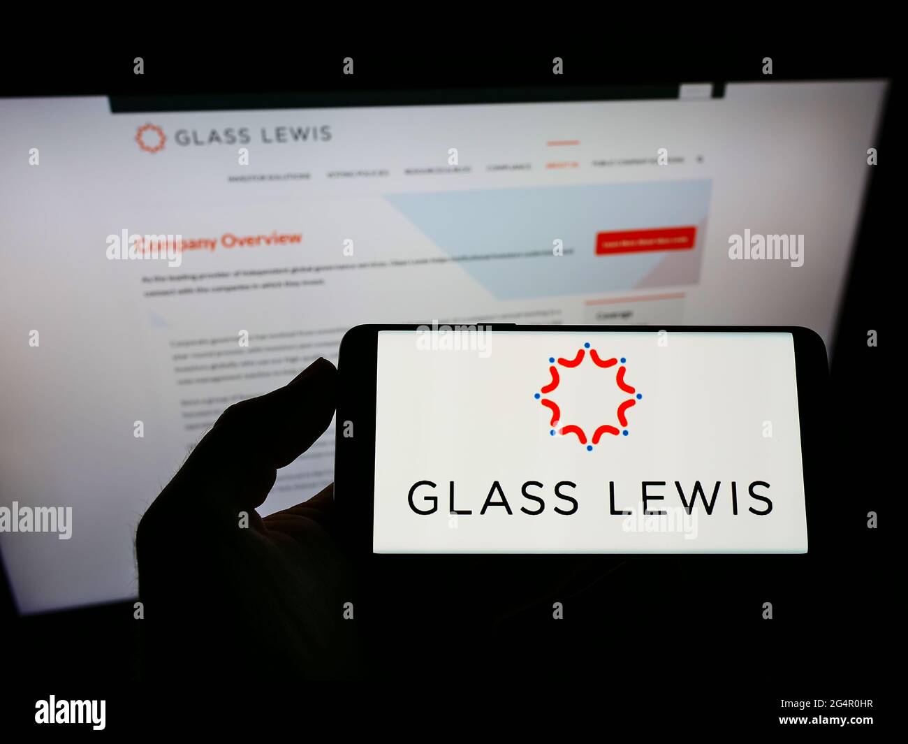 Persona che detiene smartphone con il logo della società americana di consulenza proxy Glass, Lewis Co. Sullo schermo di fronte al sito web. Mettere a fuoco il display del telefono. Foto Stock