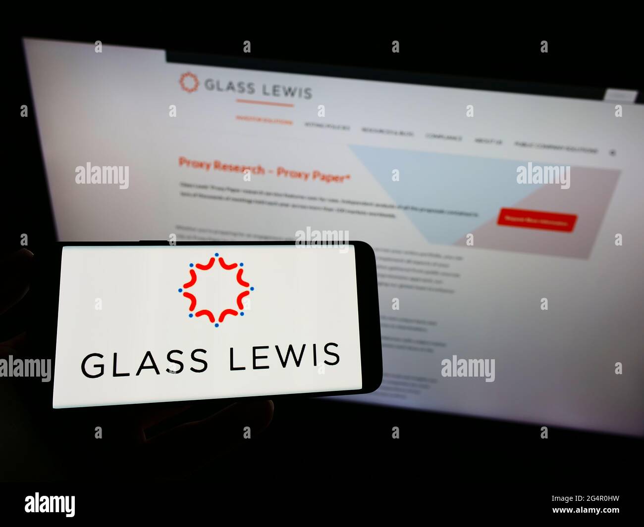 Persona che tiene il cellulare con il logo della società americana di consulenza proxy Glass, Lewis Co. Sullo schermo di fronte alla pagina web aziendale. Mettere a fuoco il display del telefono. Foto Stock