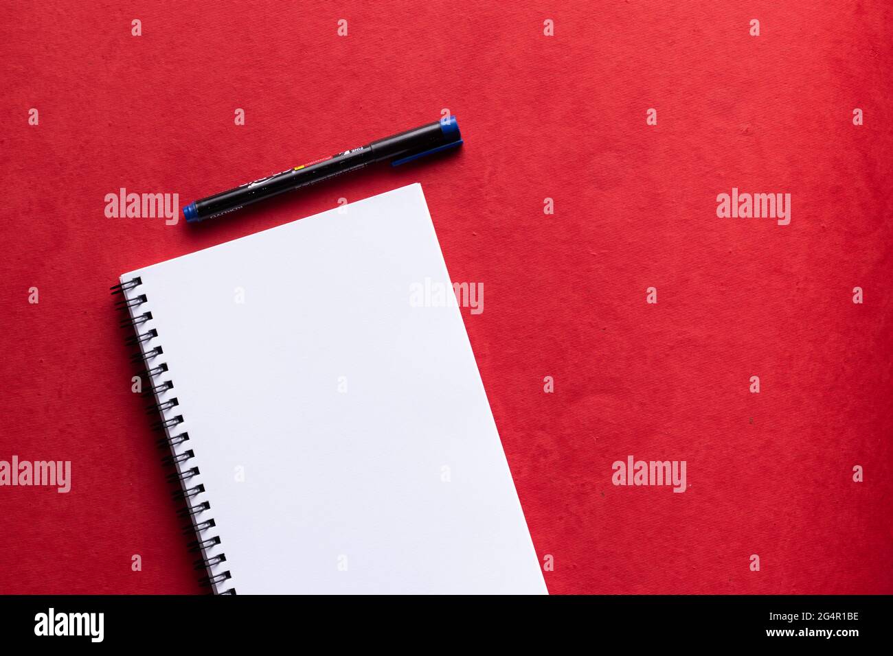 Un quaderno di carta bianca con un pennarello posizionato su uno sfondo rosso Foto Stock