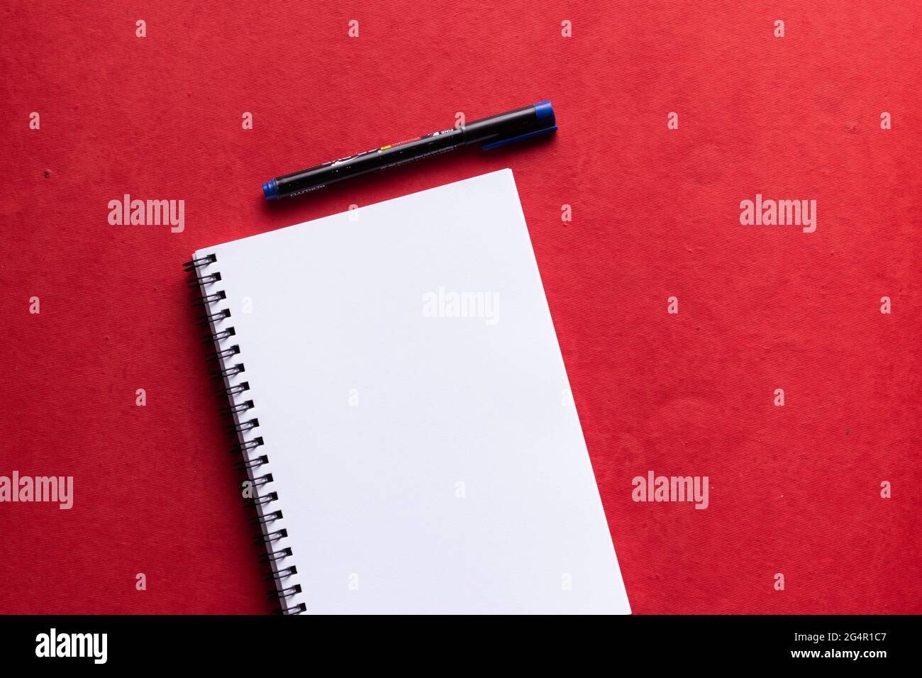 Un quaderno di carta bianca con un pennarello posizionato su uno sfondo rosso Foto Stock