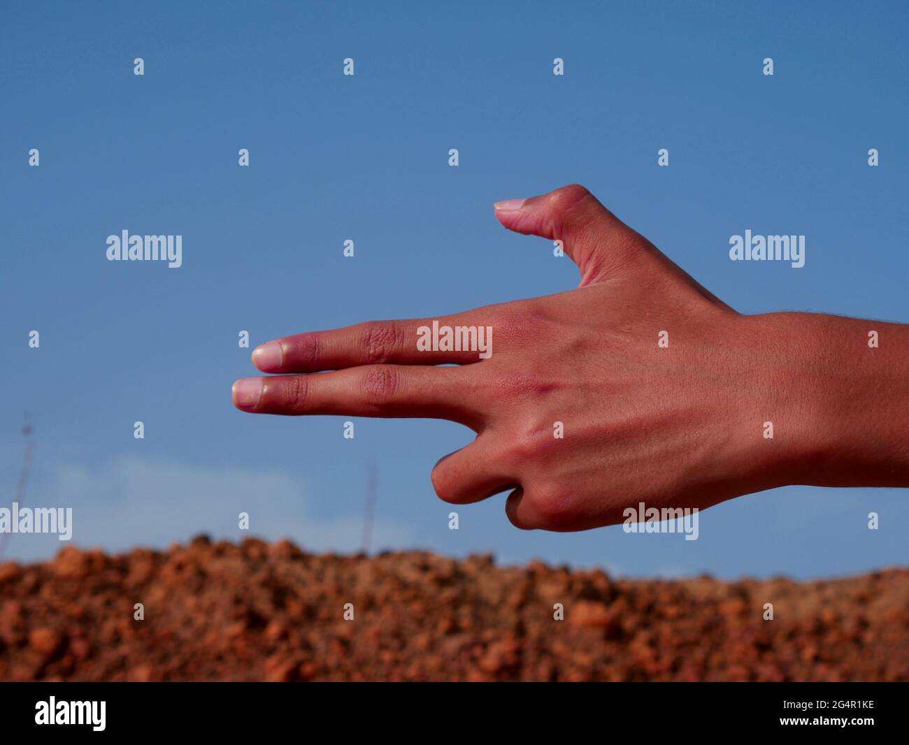 Mano del ragazzo sulla forma della pistola presentata su sfondo blu cielo. Foto Stock