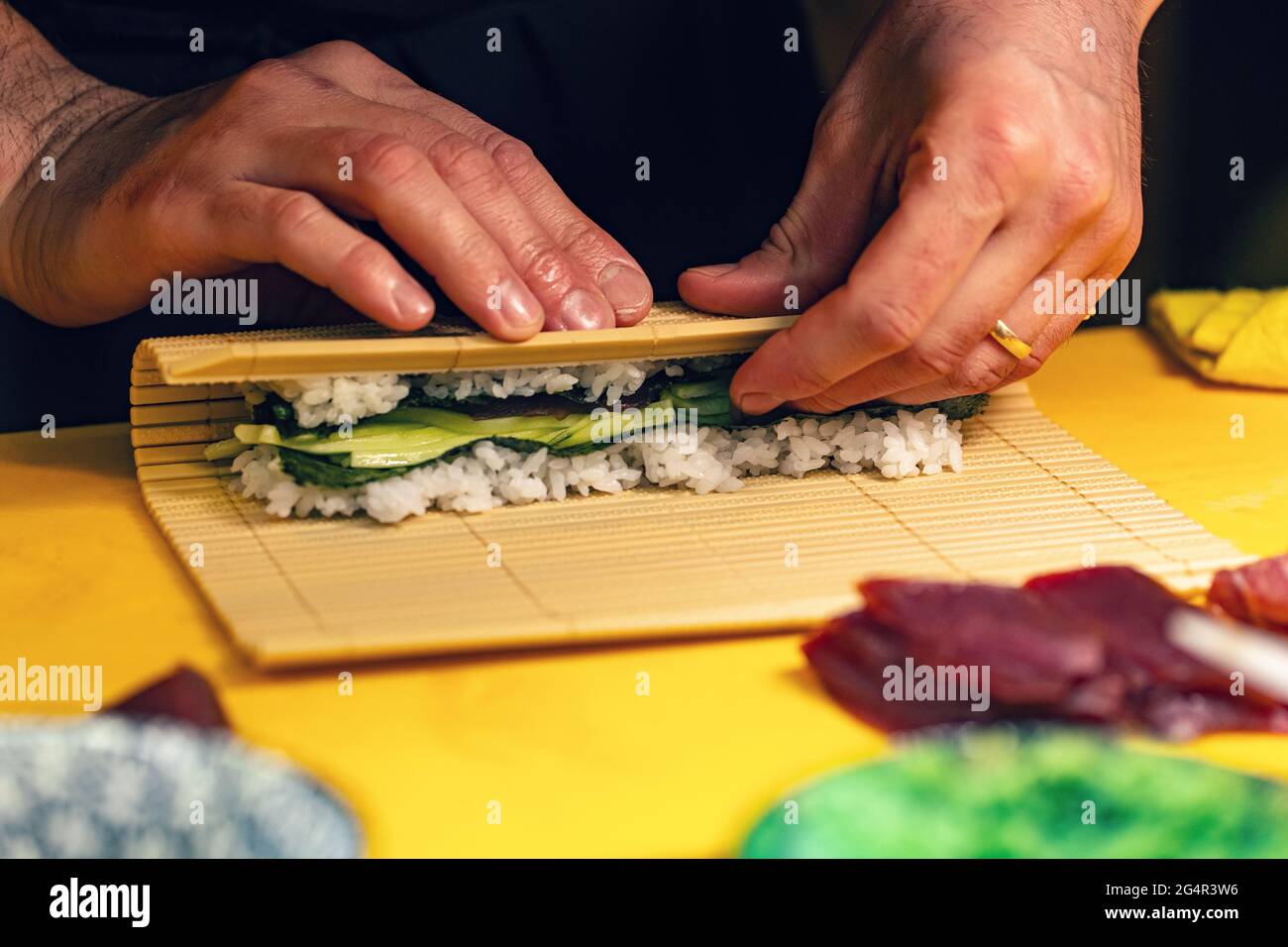 Lo chef del sushi trasforma il foglio di nori con il ripieno nel guardaroba del rotolo Foto Stock