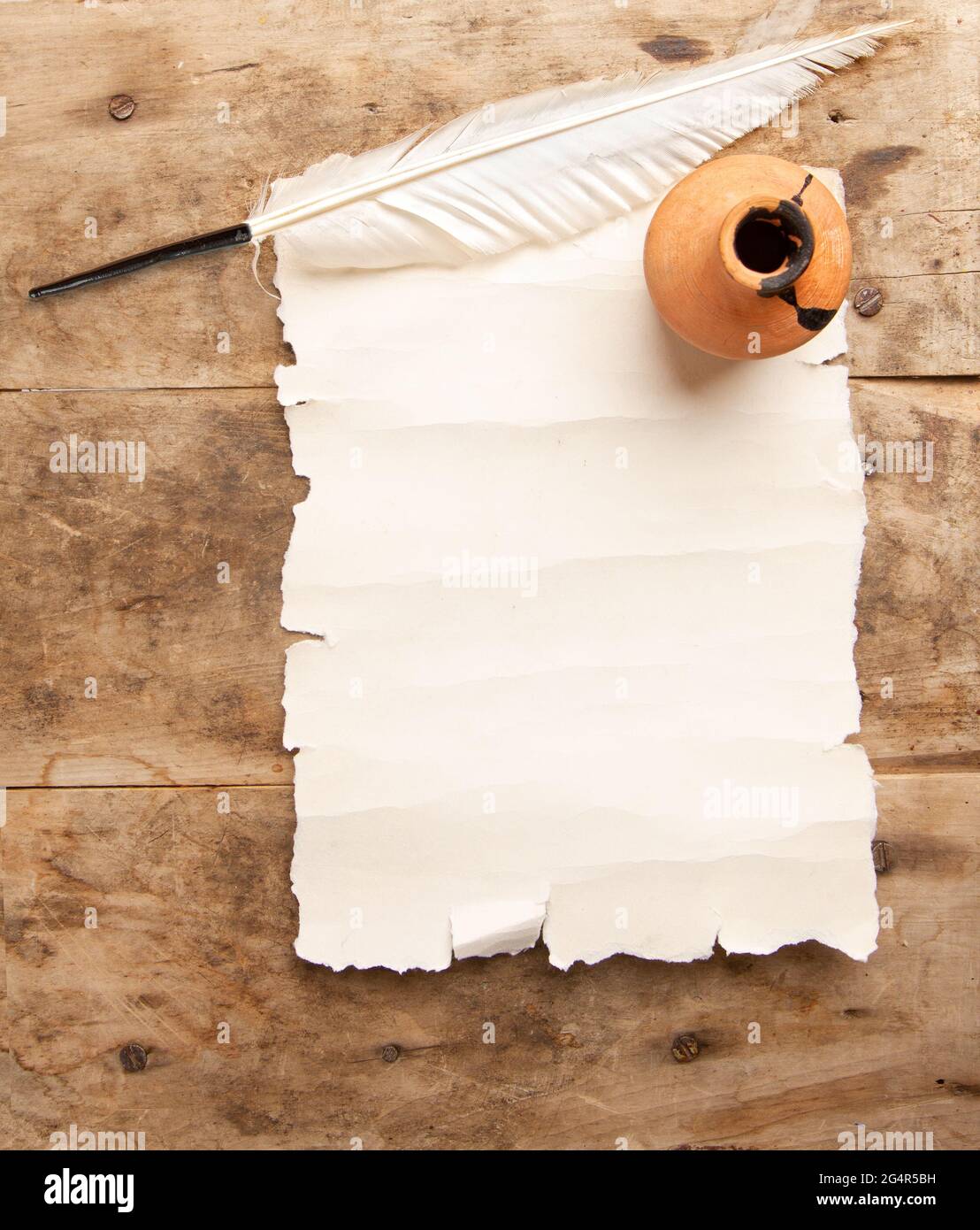 Penna trapanata bianca vintage per la scrittura di fogli di pergamena bianchi con posto per il testo e inkwell su tavolo di legno grezzo Foto Stock