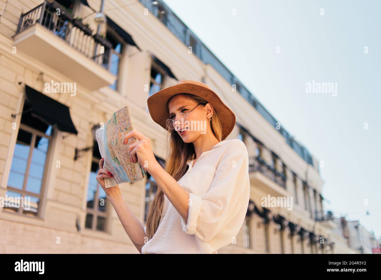 Giovane donna turistica casual in felt Hat guardando nella mappa della città sullo sfondo della vecchia architettura urbana. Il concetto di viaggio a unfa Foto Stock