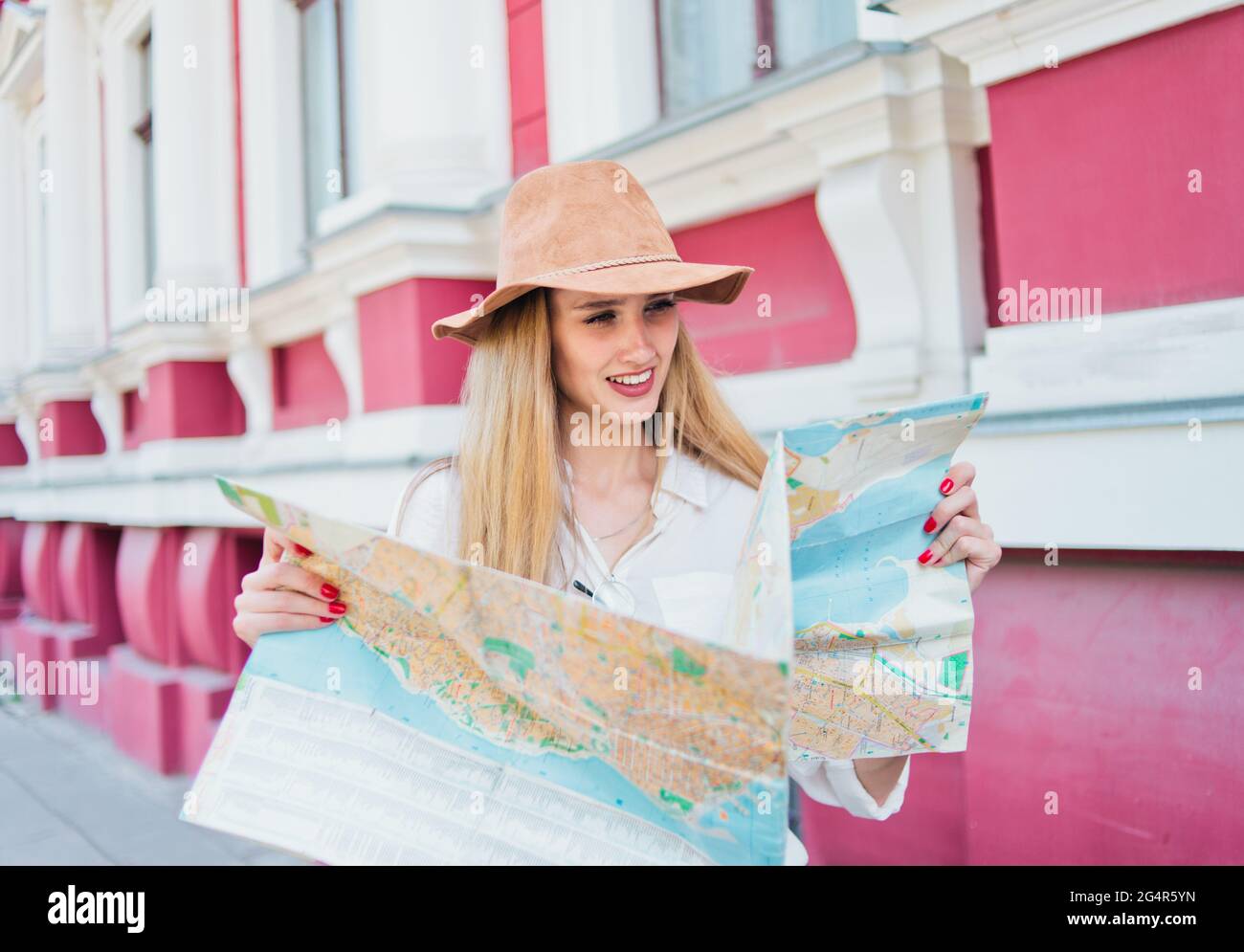 Giovane donna turistica casual in felt Hat guardando nella mappa della città sullo sfondo della vecchia architettura urbana. Il concetto di viaggio a unfa Foto Stock