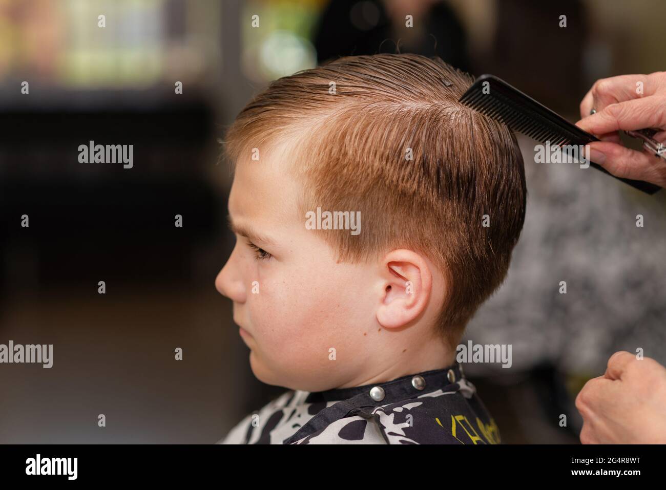 Un piccolo ragazzo carino che ottiene il taglio dei capelli dal parrucchiere al barbershop.side view.Closeup. Foto Stock