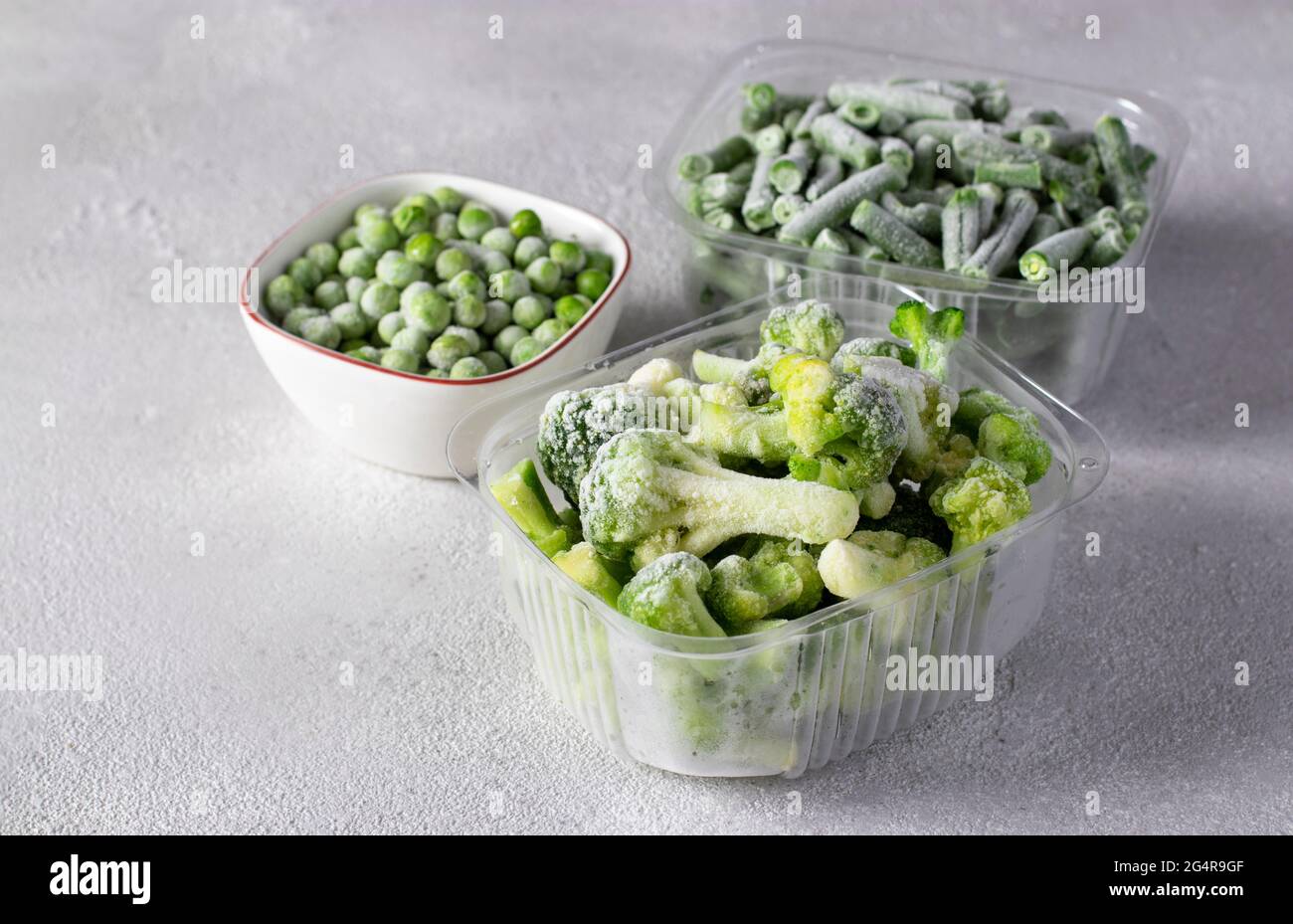 Verdure surgelate come piselli verdi, fagioli verdi e broccoli nelle scatole di conservazione sullo sfondo grigio chiaro. Foto Stock