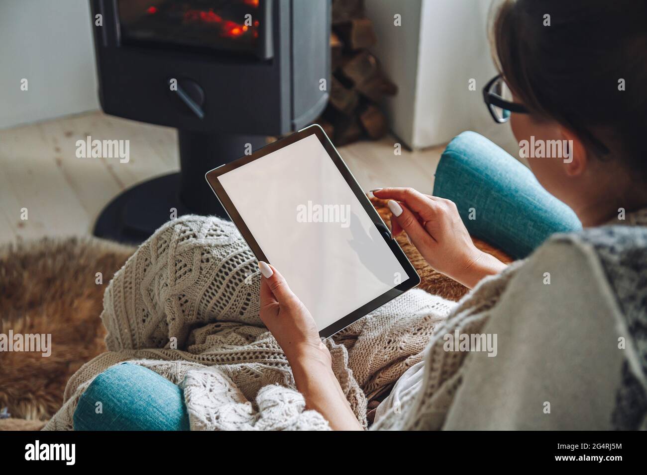donna accanto al camino, seduta in una comoda poltrona, con un caldo Foto Stock