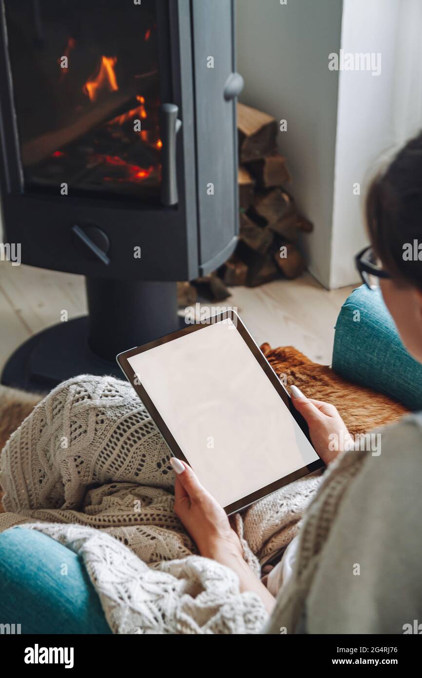 donna accanto al camino, seduta in una comoda poltrona, con un caldo Foto Stock