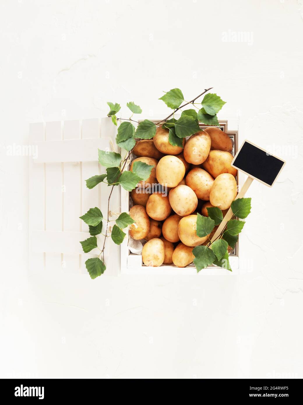 Patate da fattoria giovani, naturali, in una scatola di legno bianco e foglie su sfondo bianco. Vendita di verdure di stagione al mercato locale Foto Stock