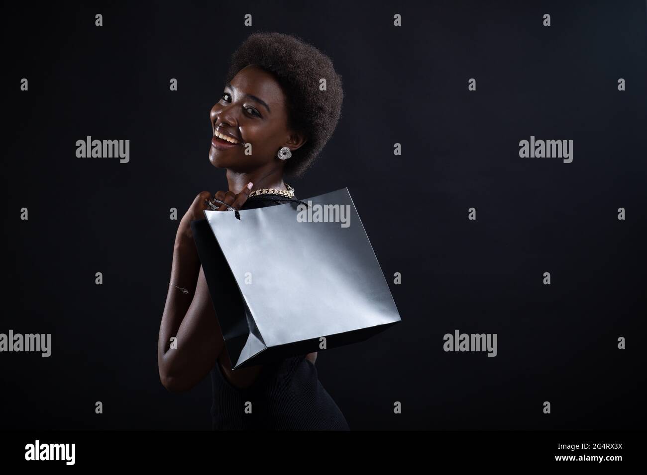 La vista posteriore della donna afroamericana con la pettinatura afro tiene le borse nere della spesa. Sconti e sconti sul mercato e Black Friday Concept. Foto Stock
