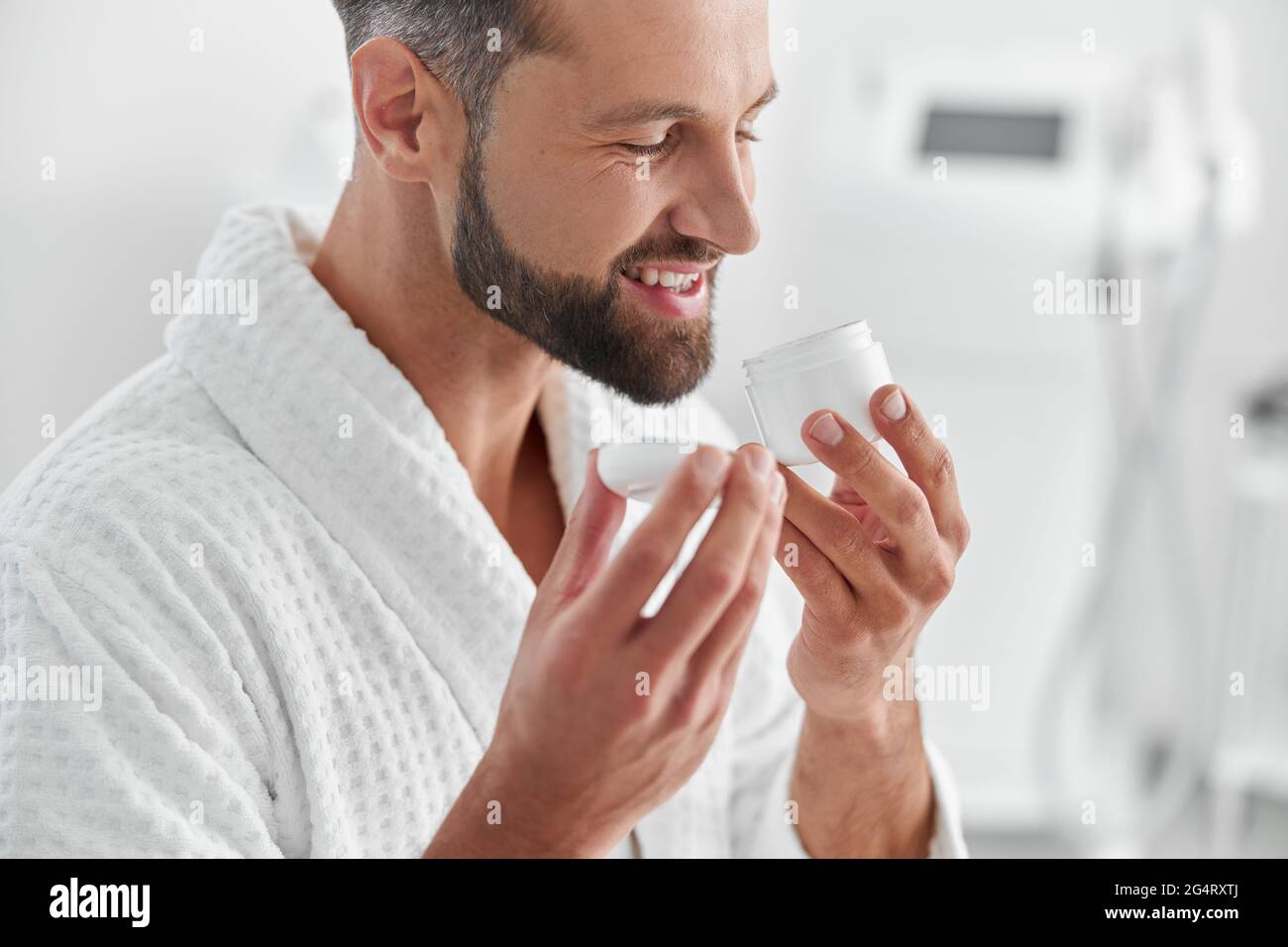 L'uomo positivo odori crema in vaso aperto prima della procedura in clinica cosmetologycal Foto Stock
