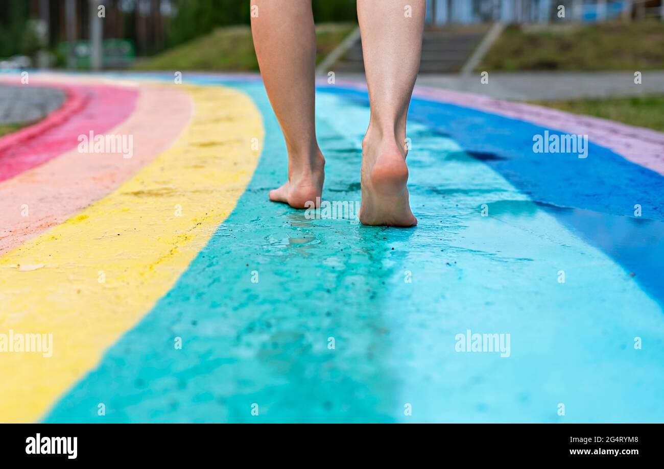 Piedi femminili vicino a piedi nudi su asfalto bagnato tracciato iridato percorso a piedi dopo la pioggia tra pozzanghere, copia spazio, amore, libertà e amicizia Foto Stock