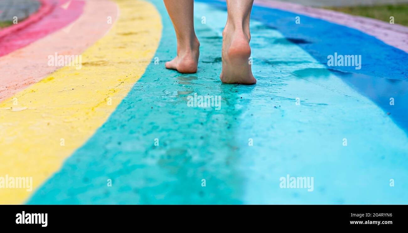 Piedi femminili vicino a piedi nudi su asfalto bagnato tracciato iridato percorso a piedi dopo la pioggia tra pozzanghere, copia spazio, amore, libertà e amicizia Foto Stock