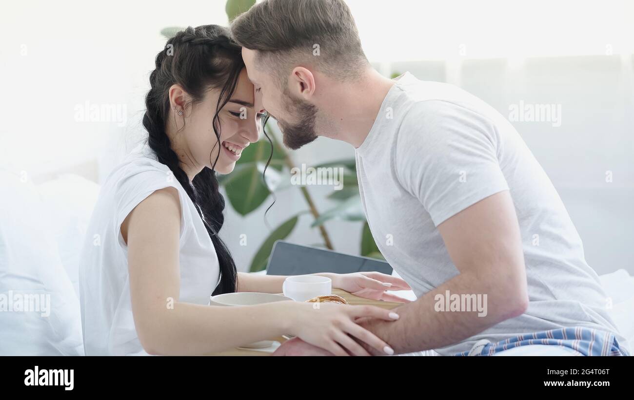 uomo bearded che porta la colazione alla ragazza felice con le trecce a letto Foto Stock