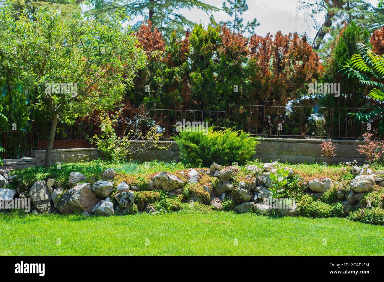 un giardino decorato con file di grandi pietre e piante, circondato da un muro di pietra e una recinzione di ferro. Foto Stock