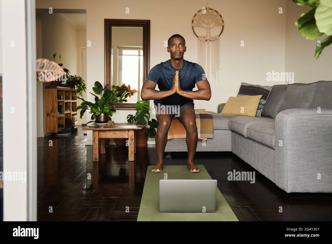 Uomo africano in posa sedia durante una lezione di yoga online Foto Stock