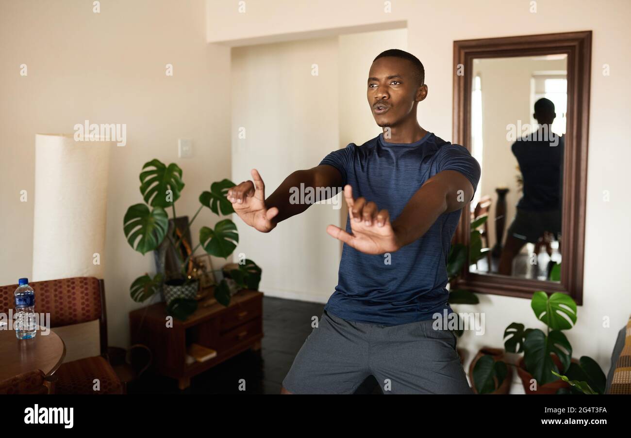 Calzare il giovane africano che pratica il Tai Chi in soggiorno Foto Stock