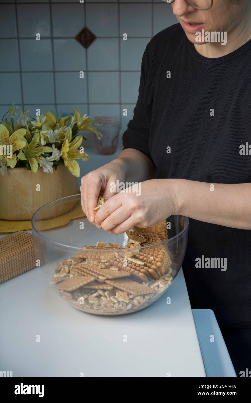 Lei sta sgretolando i biscotti. Sta facendo una torta di compleanno con biscotti e cioccolato. Torta a mosaico. Buon compleanno. Foto Stock