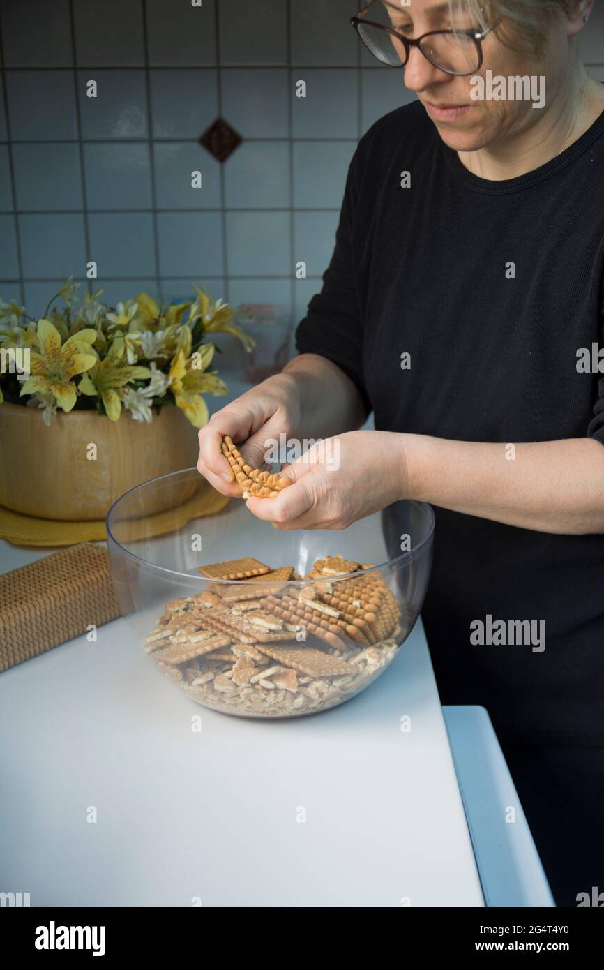 Lei sta sgretolando i biscotti. Sta facendo una torta di compleanno con biscotti e cioccolato. Torta a mosaico. Buon compleanno. Foto Stock