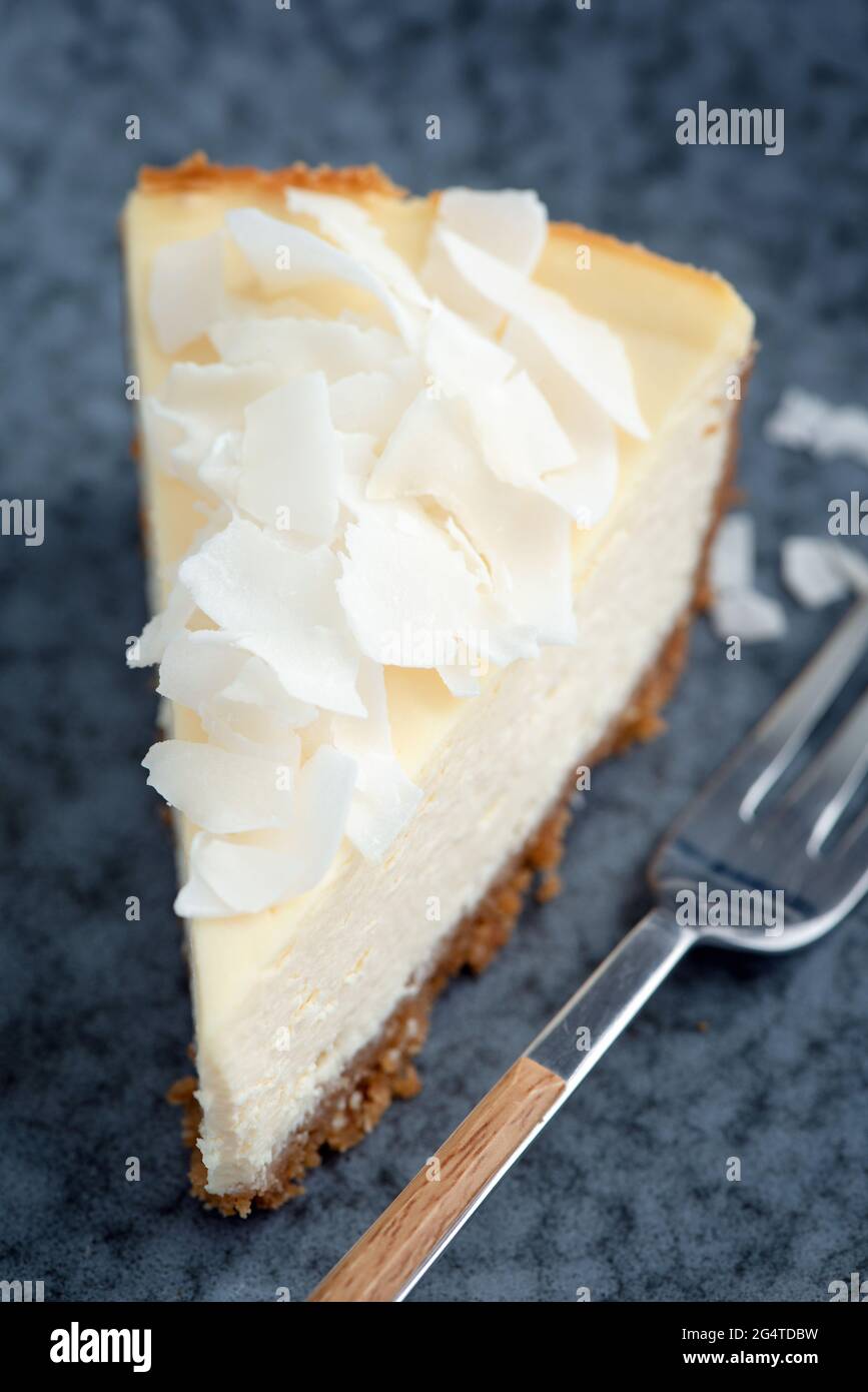 Fetta di cheesecake al cocco con fiocchi di cocco su sfondo blu, vista del primo piano Foto Stock