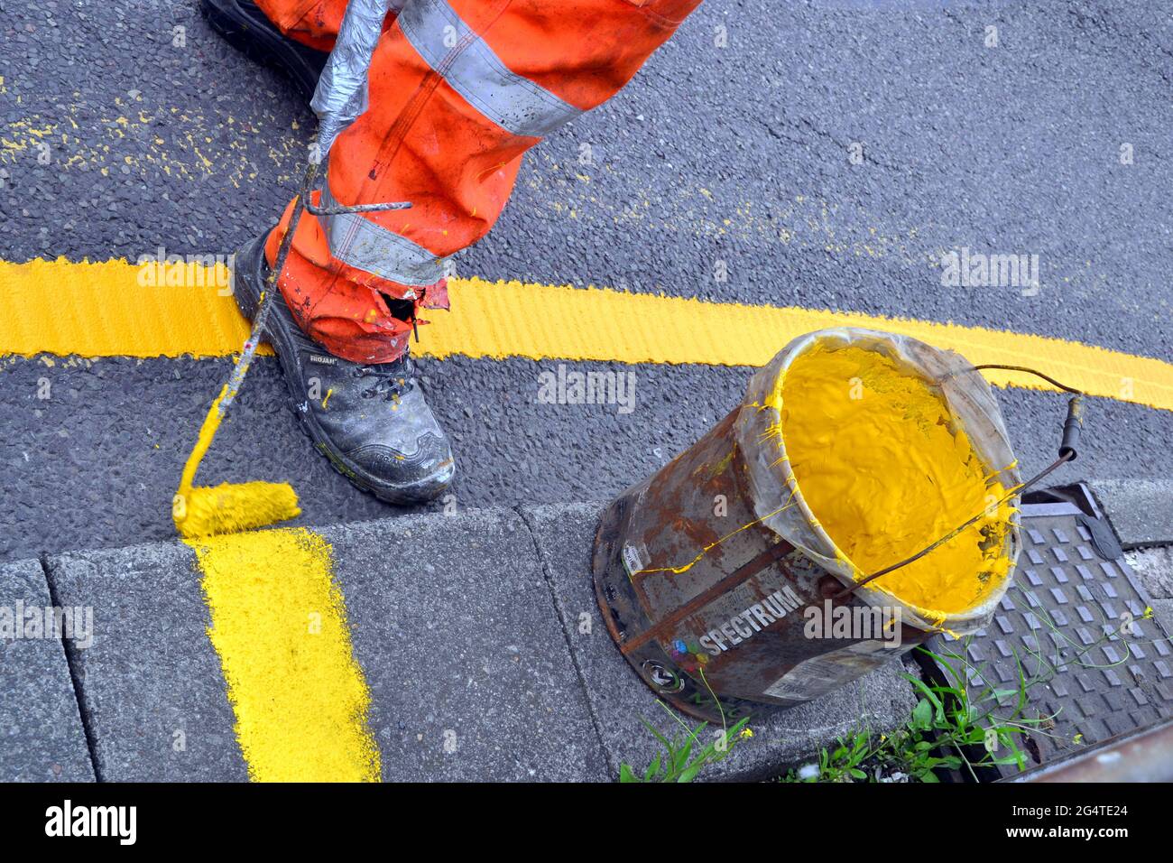 Piede di un operaio che dipinge linee gialle sulle superfici stradali accanto al vaso di vernice gialla a Manchester, regno unito Foto Stock