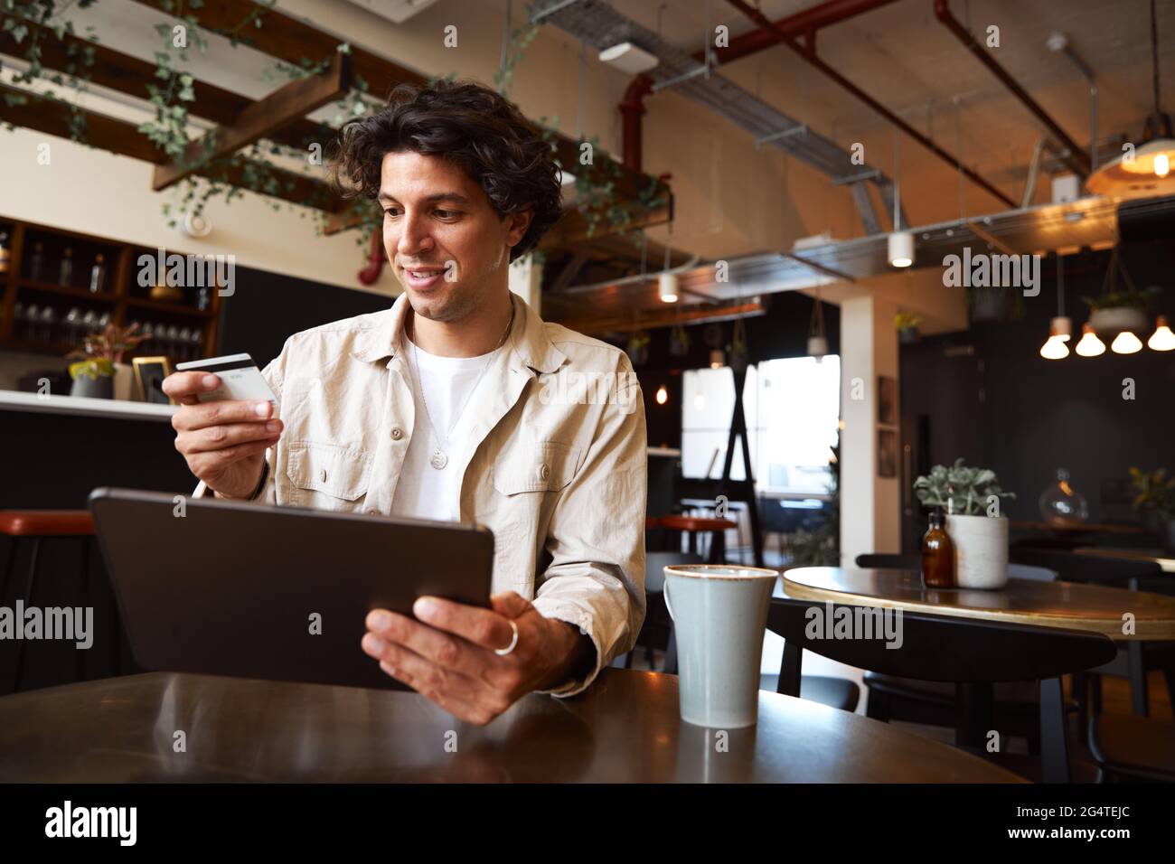 Giovane uomo a tavola nel coffee shop che effettua transazioni online con carta di credito Foto Stock