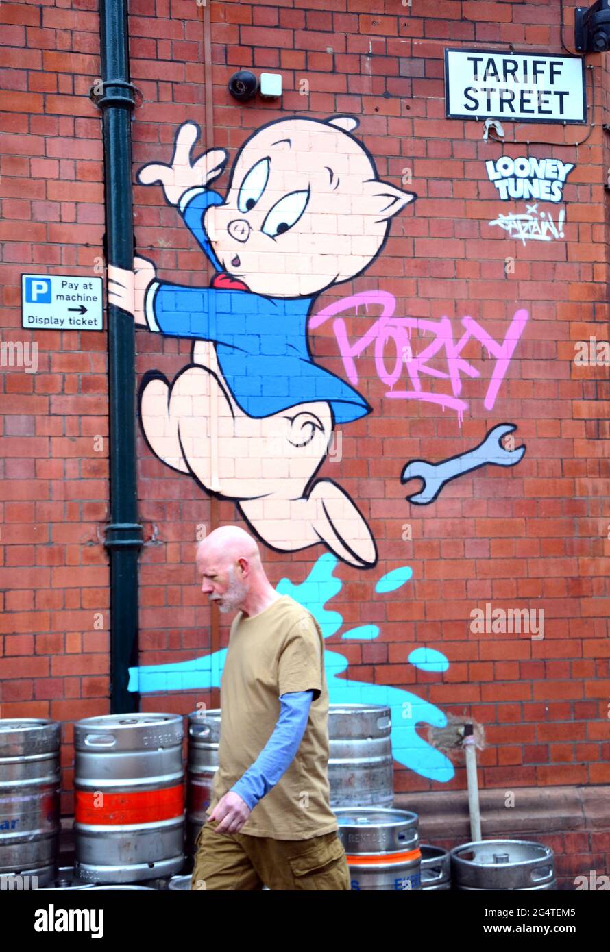 Un uomo passa accanto a un'immagine del personaggio dei cartoni animati Porky Pig, parte di un percorso artistico Looney Tunes che ha aperto a Manchester, Inghilterra, Regno Unito. Il percorso segnerà il film Space Jam: A New Legacy che sarà presto nei cinema a Manchester. Le immagini dei cartoni animati appaiono in 12 località a Manchester. Questo su Tariff Street. Foto Stock