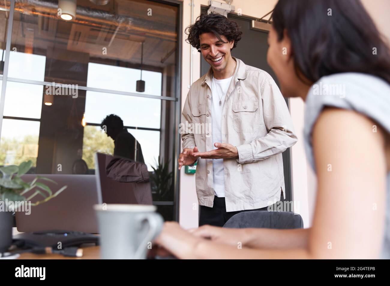 Giovane uomo e donna vestiti casualmente che lavora su computer portatili alle scrivanie che si preparano per la riunione in linea in un moderno ufficio open space Foto Stock