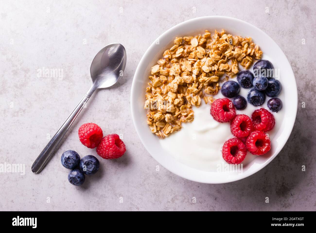 Una ciotola bianca con yogurt bianco guarnito con mirtilli maturi e lamponi e farinata d'avena alla muesli Foto Stock