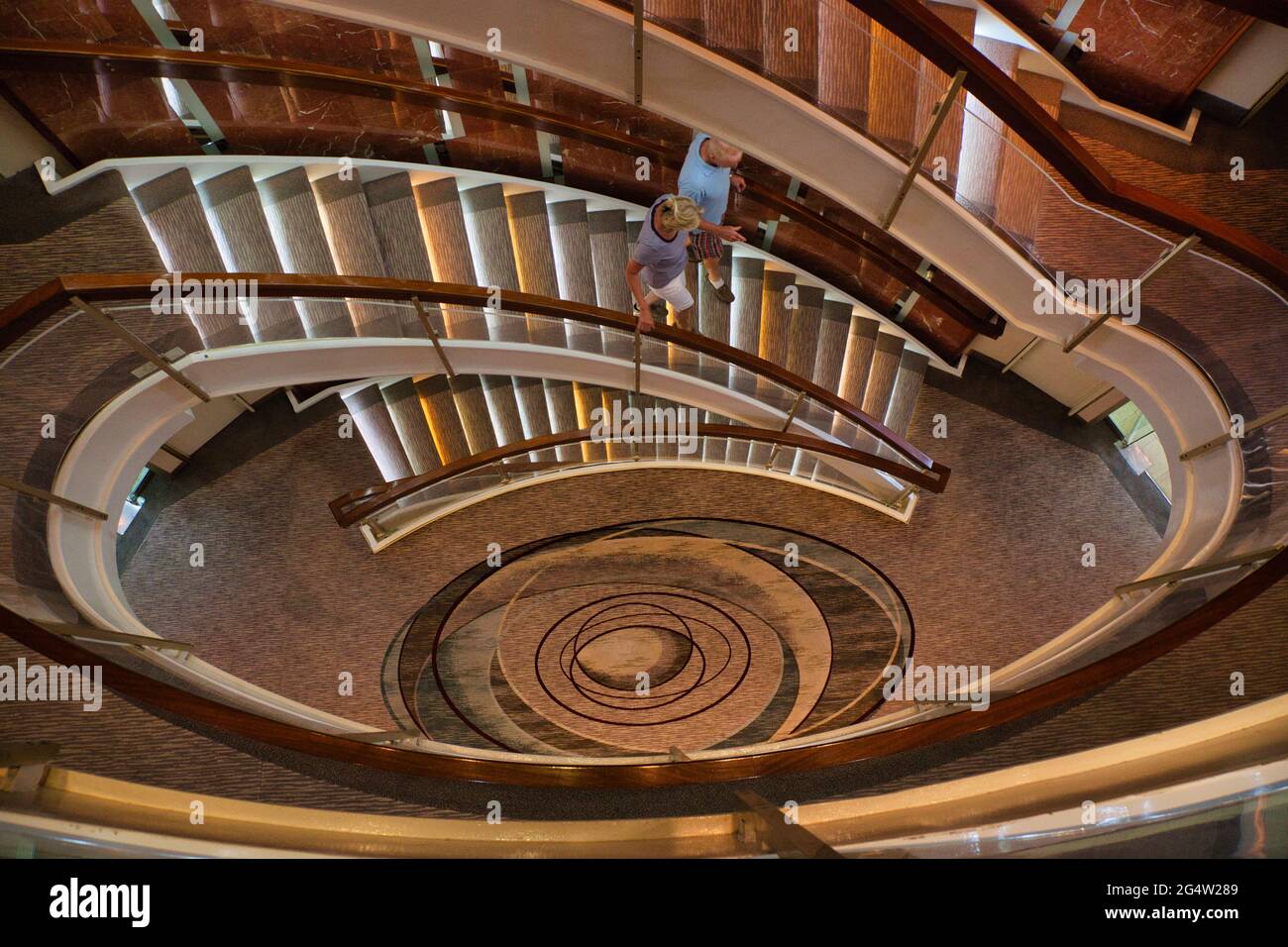 Guardando verso il basso attraverso il centro di una scala ovale su una nave da crociera con una coppia che scende le scale Foto Stock