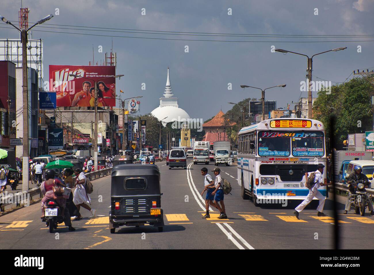 Vista lungo una strada principale con traffico e un passaggio pedonale con persone su, vicino a Columbo, con semafori, guardie e la cupola del tempio Foto Stock