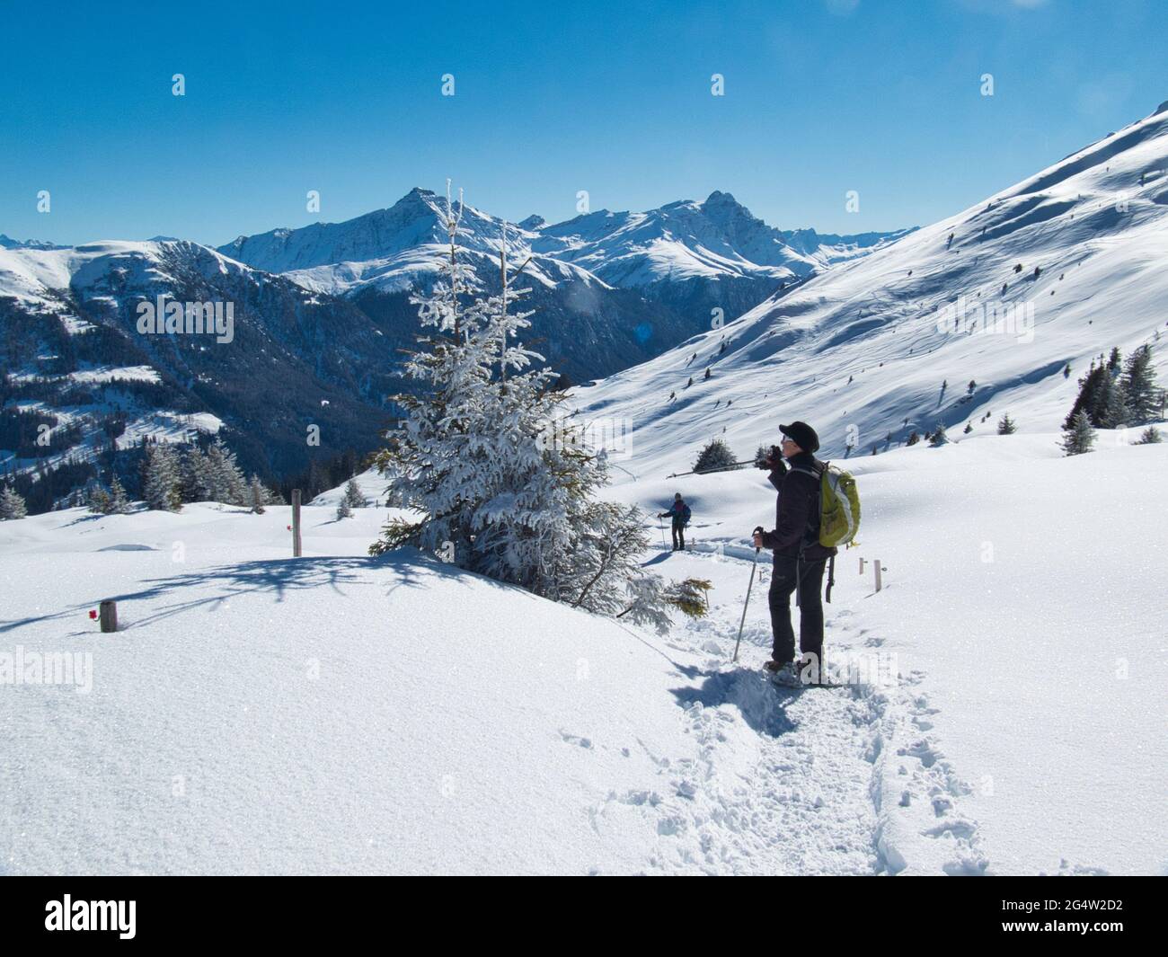 Una donna che cammina con le racchette da neve si ferma per ammirare la vista della valle di Safeiennel Cantone di Graubunden, nelle Alpi svizzere Foto Stock