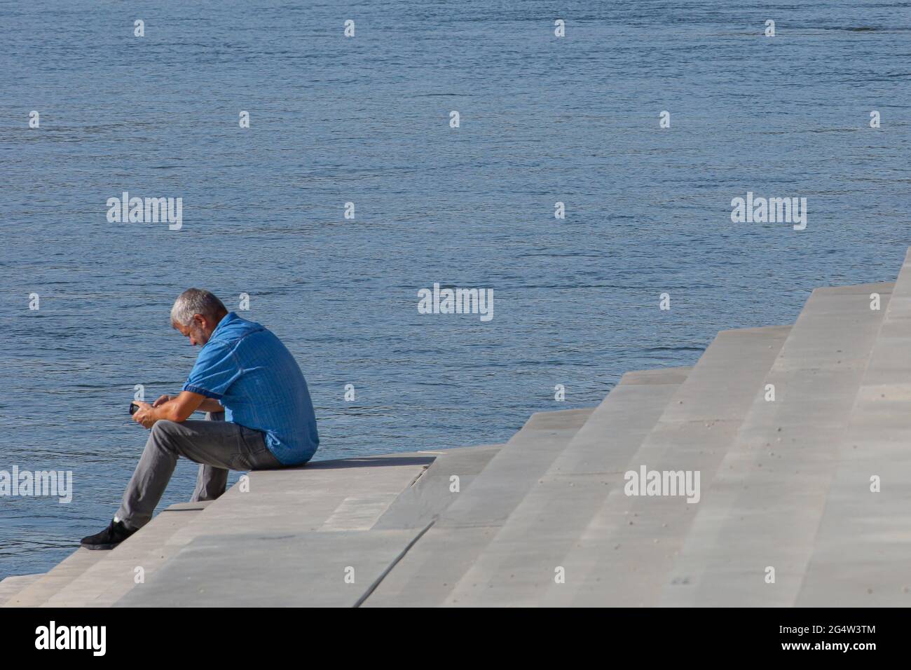 Neuwied, Germania - 6 maggio 2020: Uomo con una camicia blu seduto sulle scale vicino all'acqua - Corona causa vacanze a casa Foto Stock