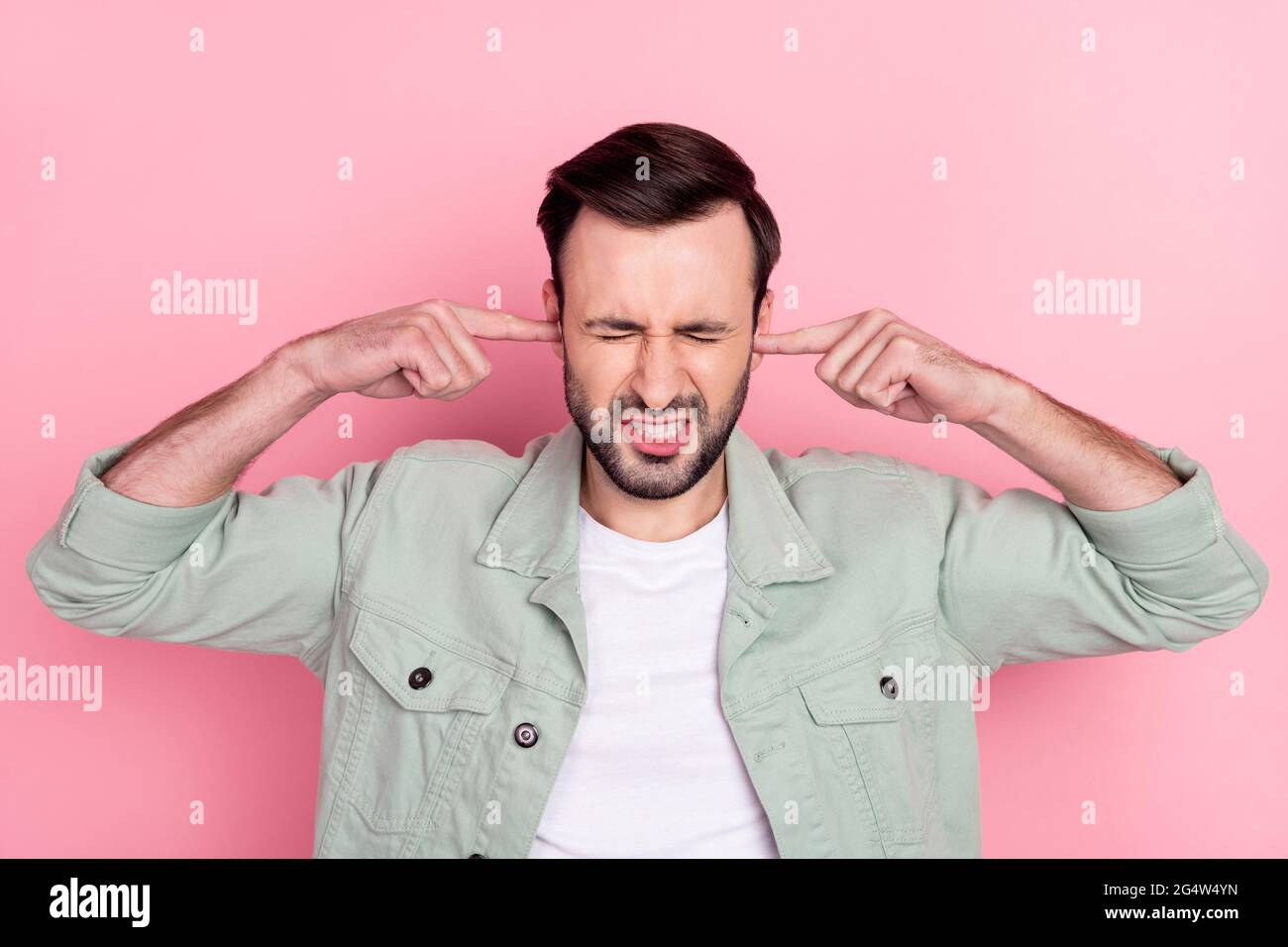 Foto di bel brunetto stressato uomo copertura orecchie indossare camicia grigia isolato su sfondo colore rosa pastello Foto Stock