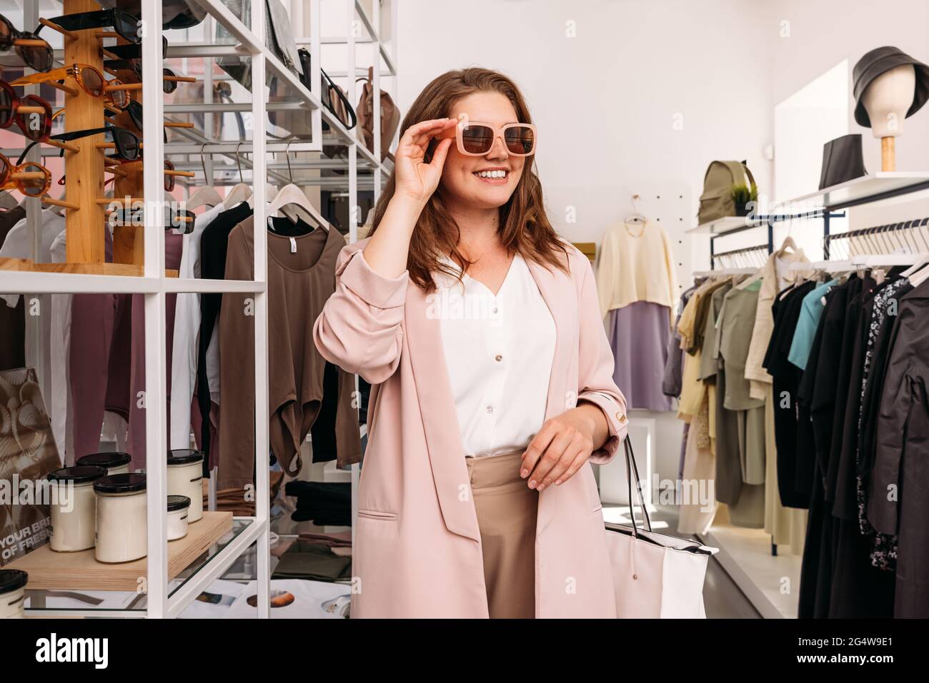 Donna felice più taglia in piedi in un piccolo negozio di moda. Allegra donna acquirente indossare occhiali da sole in una boutique. Foto Stock